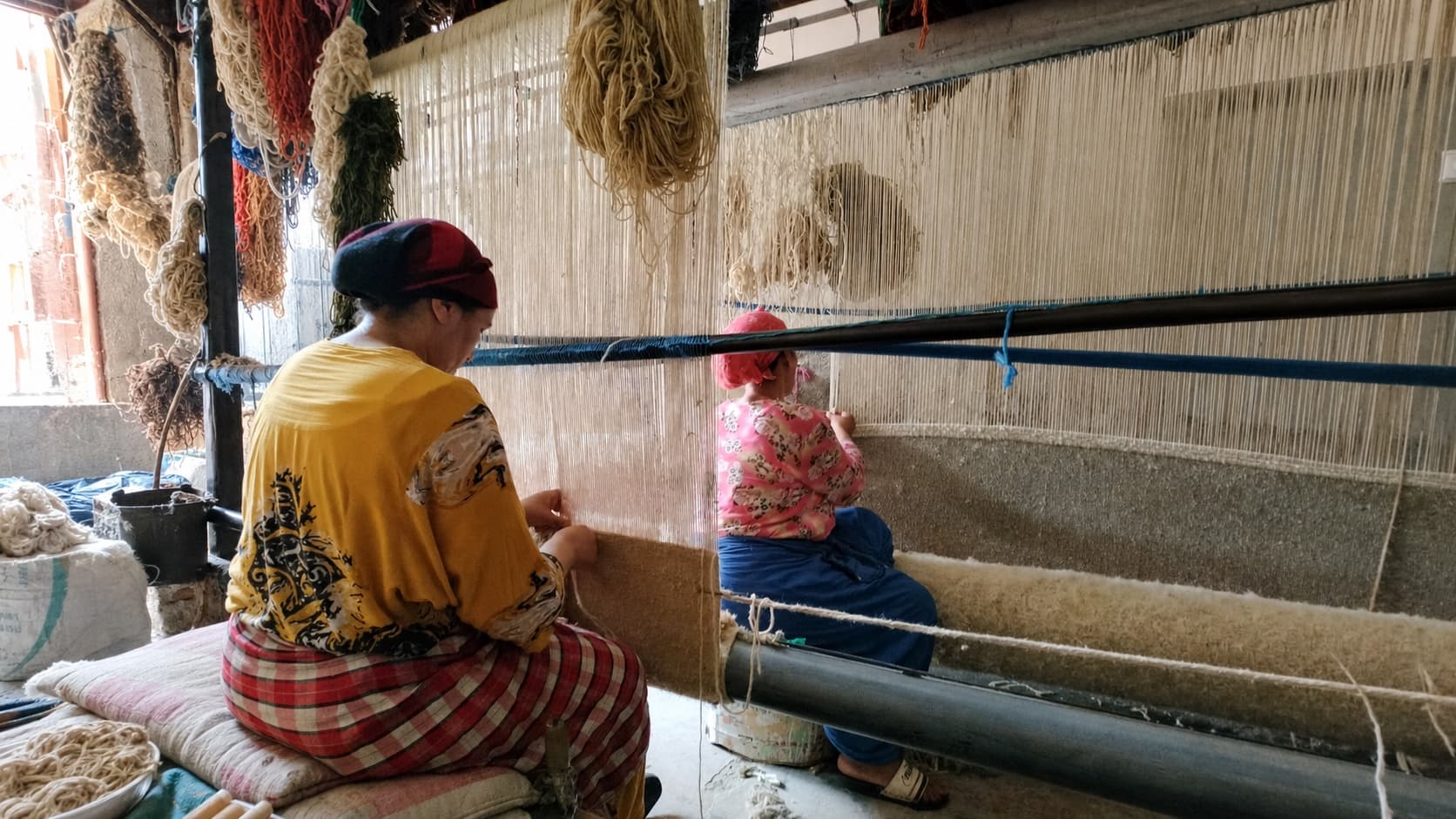 Two craftswomen hand-weave a rug on a traditional loom in Morocco