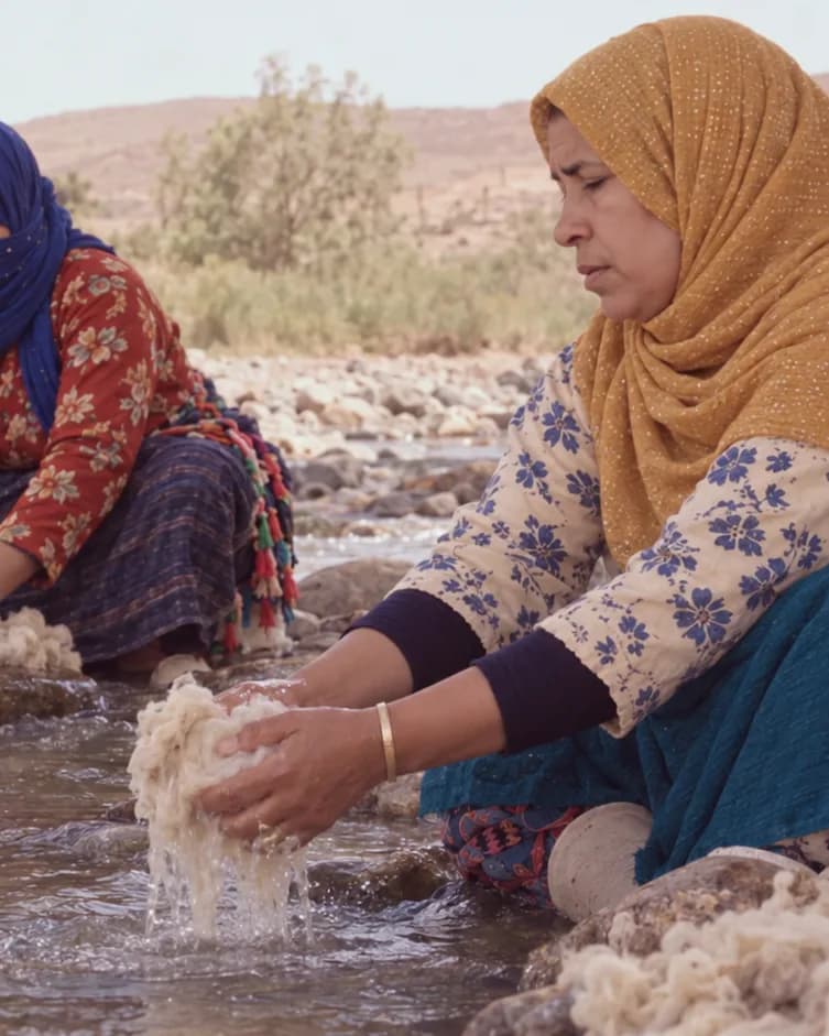 Three craftswomen wash sheep’s wool by hand in an Atlas river